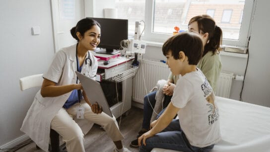 Female pediatrician discussing with mother and son over tablet PC in examination room at clinic