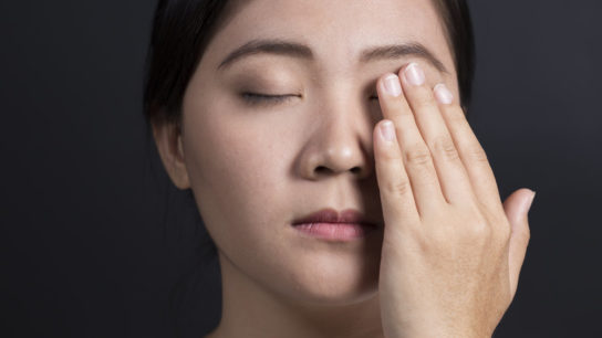 Woman holds hand up to pain behind eye