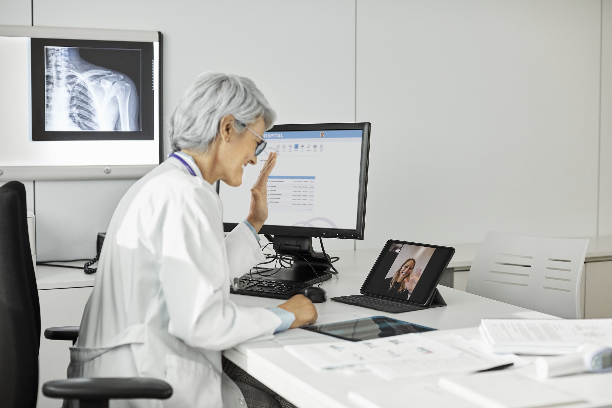 Female doctor waving hand while giving telehealth consult