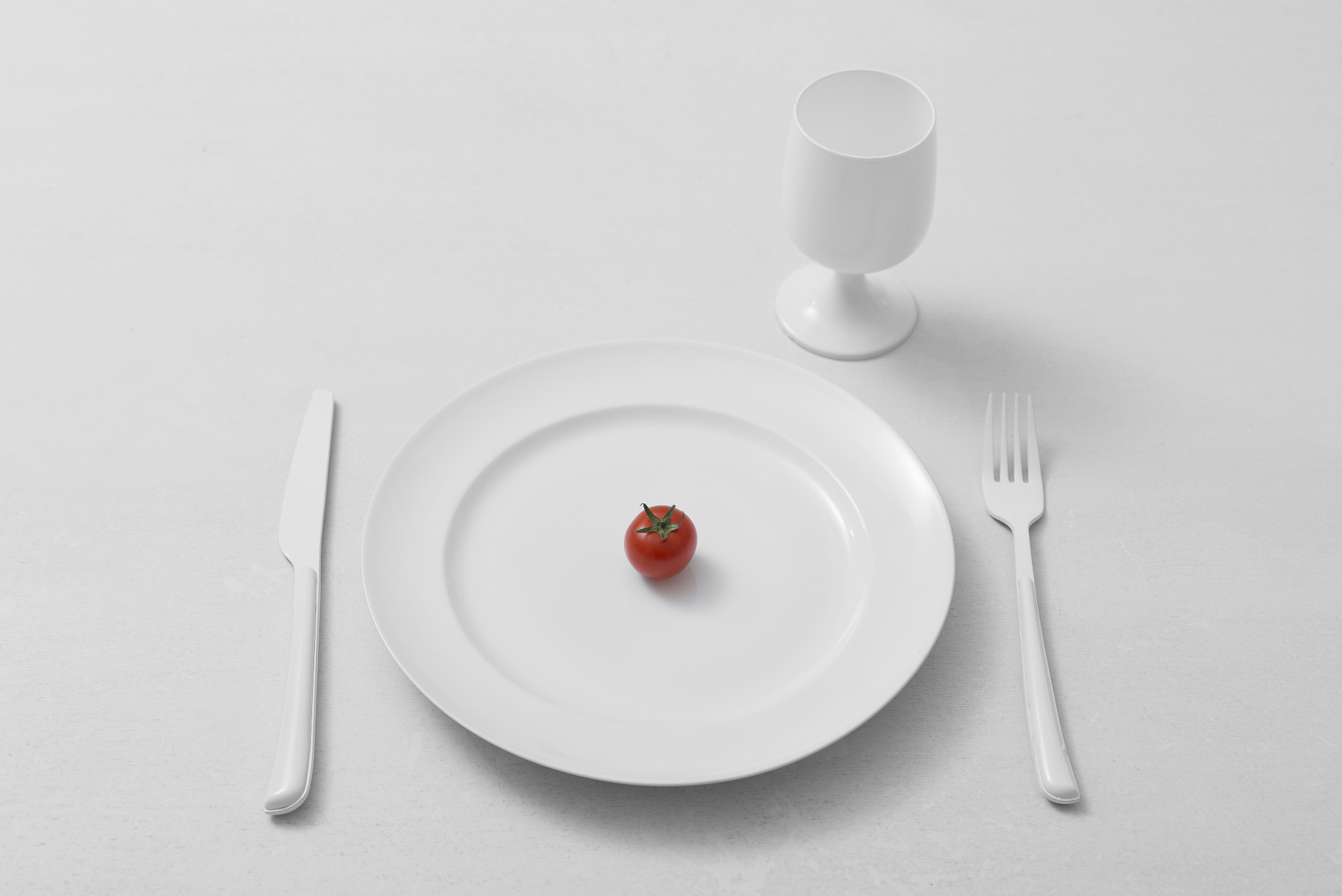 High Angle View Of white glass, fork, knife and plate with a cherry tomato on a table