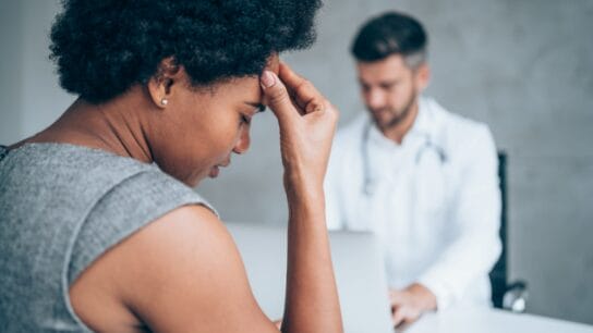 African-american-woman-sitting-opposite-the-doctor-in-his-office-and-holding-her-head-with-hand.