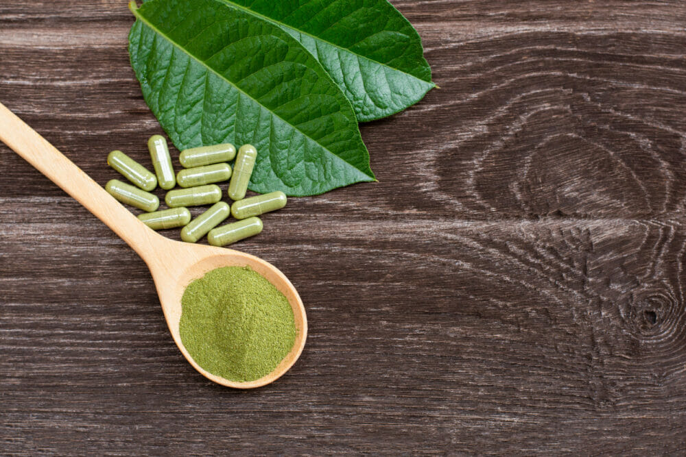 Flat-lay-top-view-of-fresh-green-kratom-leaf-with-kratom-powder-isolated-on-wooden-table-background.