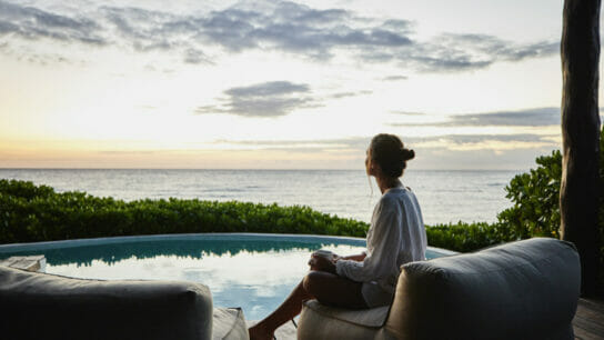 Wide_shot_of _woman_watching_sunrise_while_sitting_poolside_at_luxury_suite_at_tropical_resort.