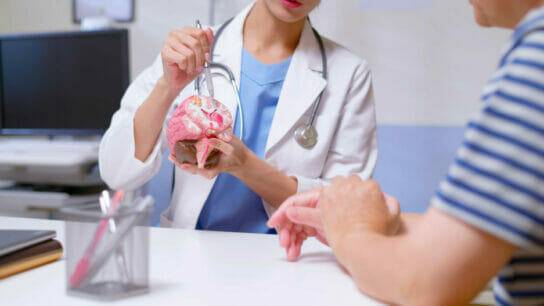 Closeup_of_young_female_doctor_with_white_coat_and_stethoscope_pen_pointing_and_explaining_conditions_related_to_brain_model_to_man_at_clinic.