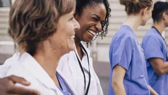 Happy-female-physician-with-arm-around-colleague-outside-hospital