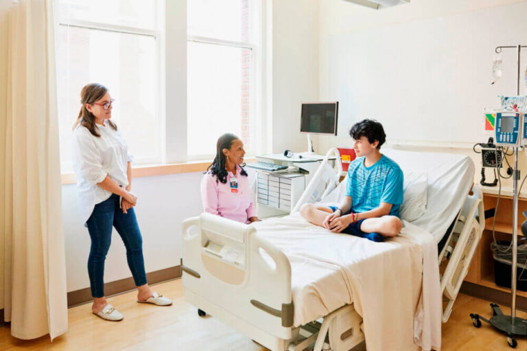 Wide-shot-of-senior-female-doctor-consulting-with-teenage-boy-during-visit-to-hospital-emergency-room.