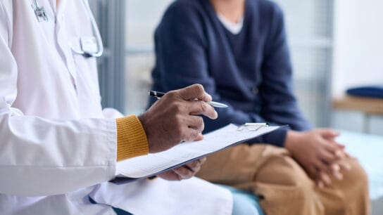 Side-view-closeup-of-Middle-Eastern-doctor-holding-clipboard-while-consulting-child-in-clinic-copy-space
