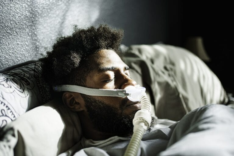 Athletic Young African American Man in His Twenties Sleeping Peacefully Using a CPAP Machine (contenuous positive air pressure) in a Dark Bedroom